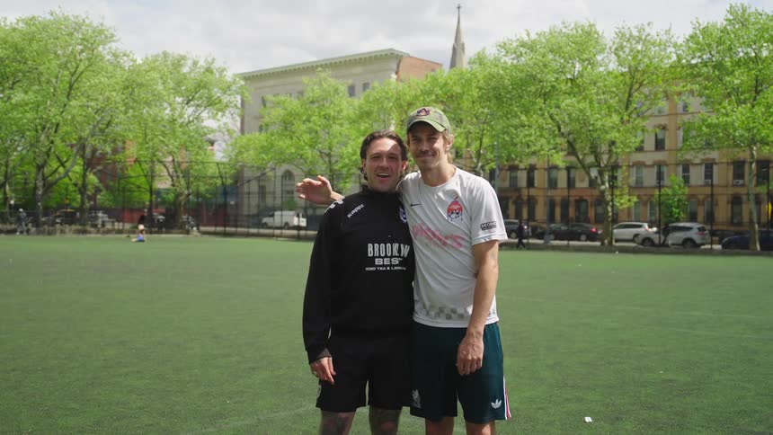 Portrait of two male friends and teammates smiling together on a city soccer field