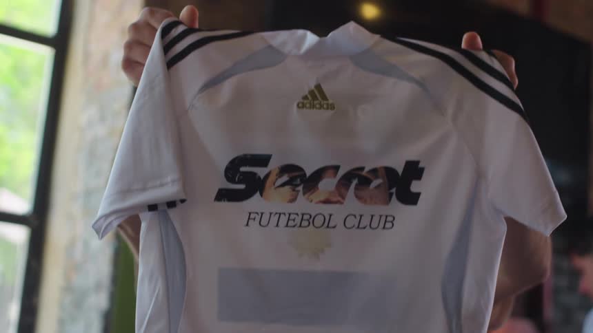 A man uses a heat press to customize a soccer jersey and proudly shows off the finished product to a friend in his workshop