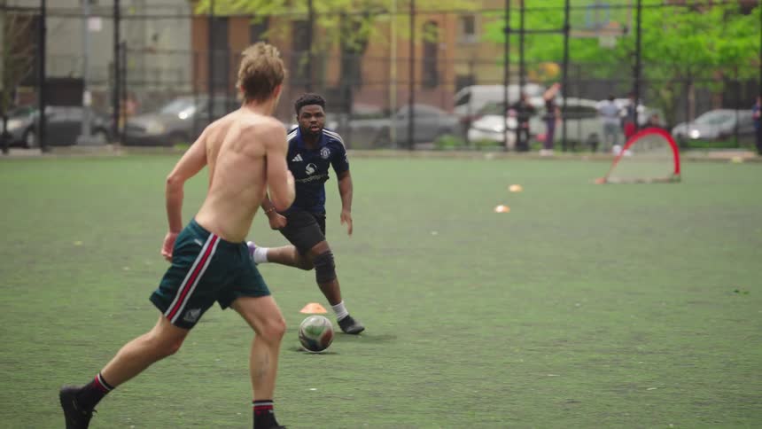 A skilled soccer player dribbles the ball past his opponents in slow motion during a pickup game on an urban turf field