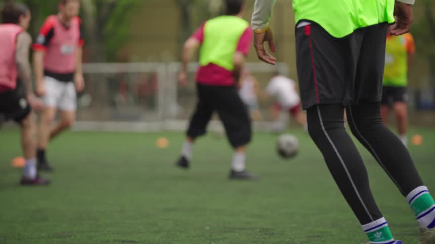 Men in colorful jerseys play a competitive game of soccer in slow motion on an urban park field