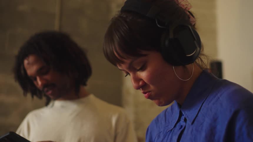 A female DJ smiles as she puts on her headphones to begin mixing music in her studio