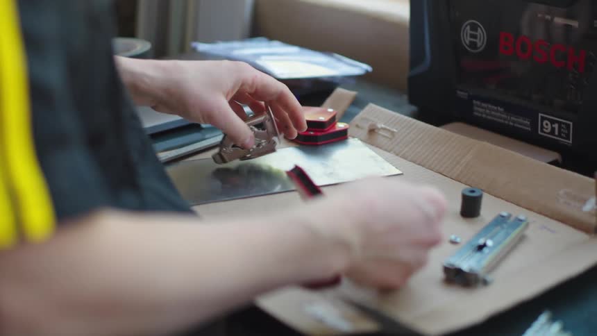 A focused young woman in a workshop carefully assembles small mechanical parts and magnets on her workbench in slow motion