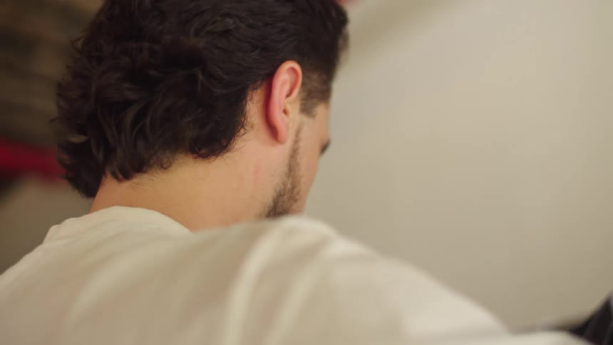 A young man browses through a rack of vintage clothing and carefully inspects a sports jersey in slow motion