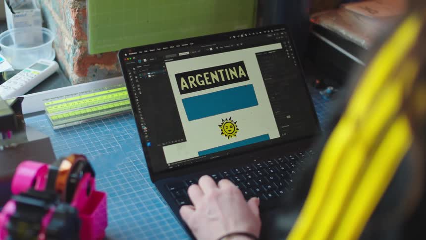 Over-the-shoulder view of a graphic designer creating a stylized and animated Argentinian flag on a laptop