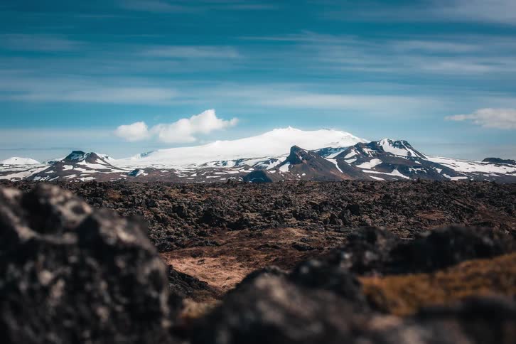 A stunning timelapse of clouds drifting over the majestic, snow-capped Snaefellsjokull volcano and glacier in Iceland, viewed from a rugged lava field