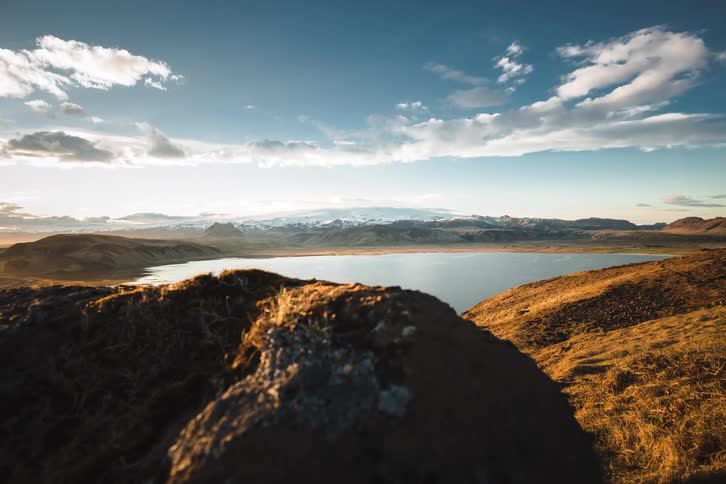 A slow dolly shot reveals a majestic Icelandic landscape with a tranquil lake and distant snow-capped mountains at sunrise