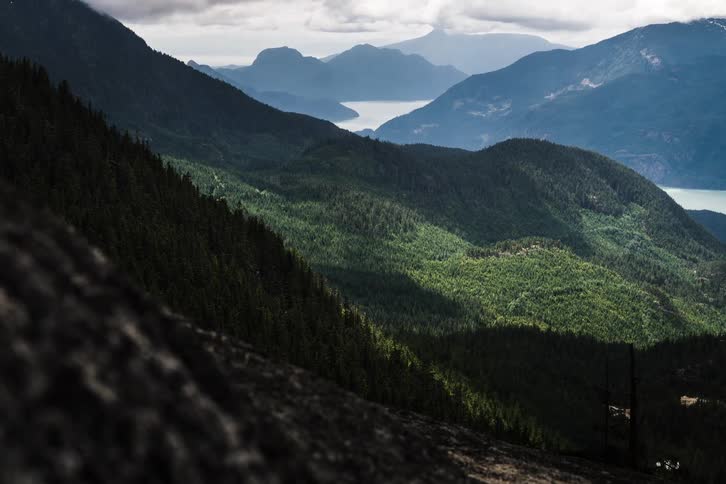 Time-lapse of shadows from moving clouds sweeping across a vast, lush green forest and mountain valley