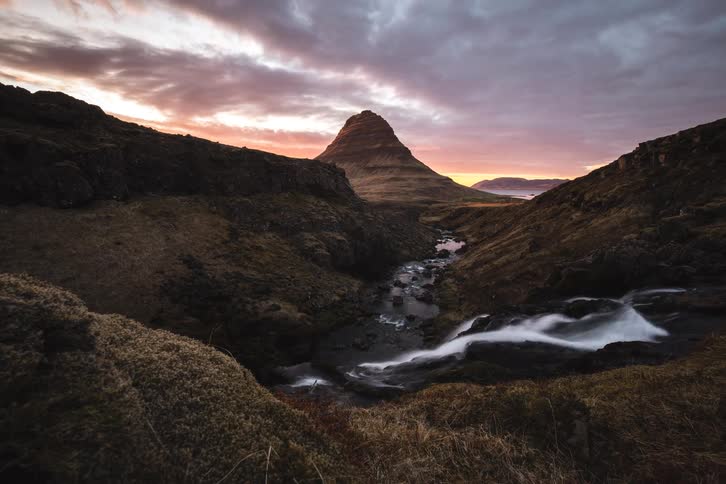 A majestic dolly shot reveals the iconic Kirkjufell mountain and Kirkjufellsfoss waterfall in Iceland during a dramatic sunset time-lapse