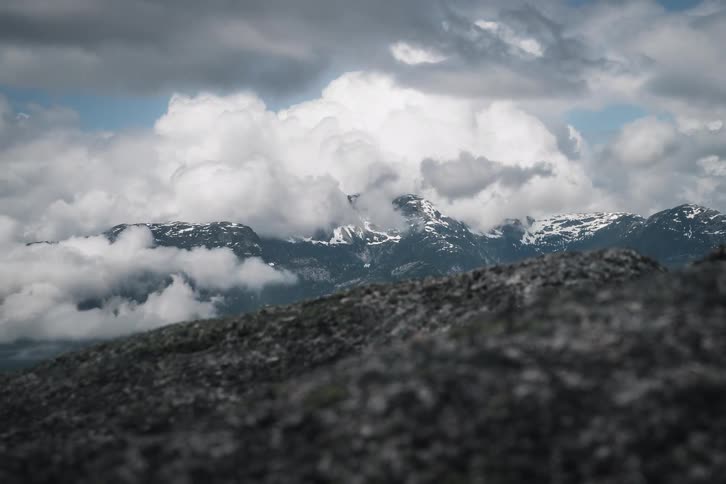A dramatic time-lapse of clouds rolling over snow-capped mountains as seen from a rocky summit