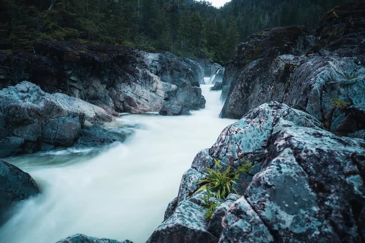 A smooth, long-exposure timelapse captures a powerful river surging through a dramatic and rocky canyon surrounded by a dense forest