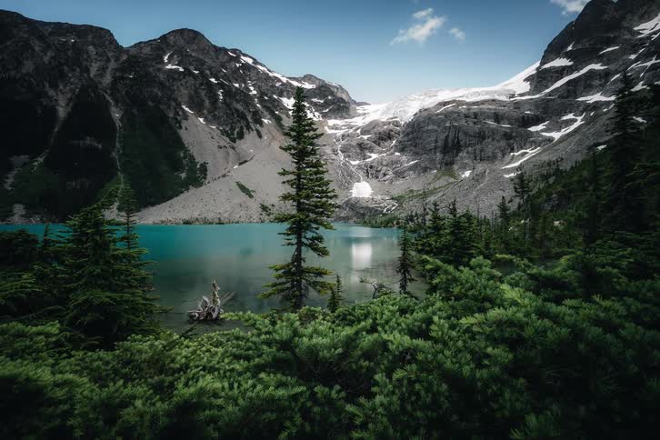 A stunning timelapse of a turquoise alpine lake surrounded by snow-capped mountains and a glacier, with sunlight and clouds moving across the landscape