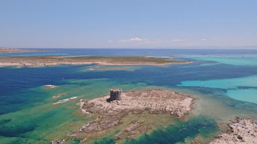 A stunning aerial view of a historic stone tower on a small island surrounded by crystal-clear turquoise and blue ocean waters