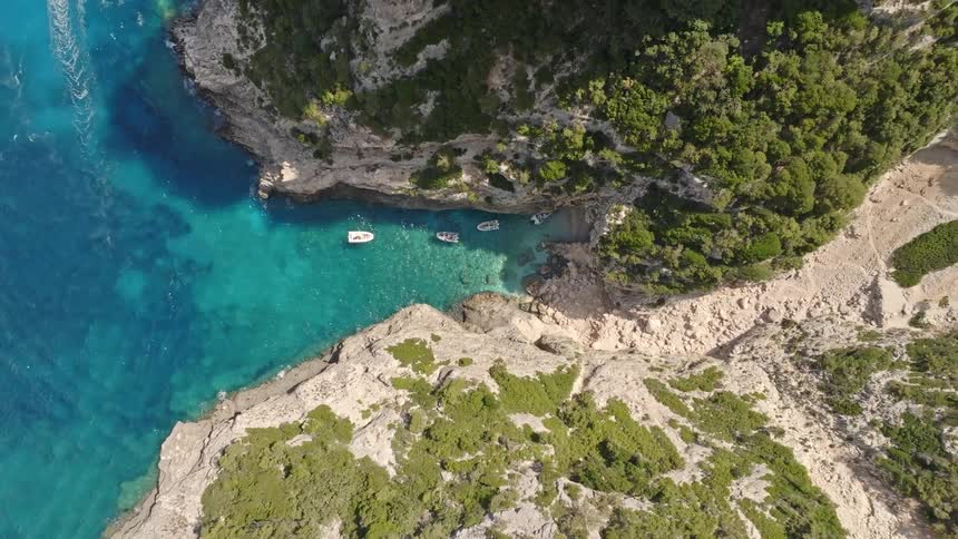 A stunning top-down aerial view slowly ascends over a hidden cove where boats rest on crystal-clear turquoise waters