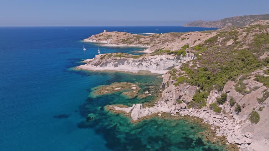 Ascending aerial shot of a beautiful, rugged coastline with turquoise water, white rock cliffs, and a distant historic tower