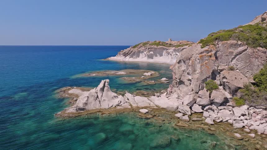 An aerial view pulls back over a pristine turquoise bay to reveal the stunning rocky coastline of a secluded Mediterranean island