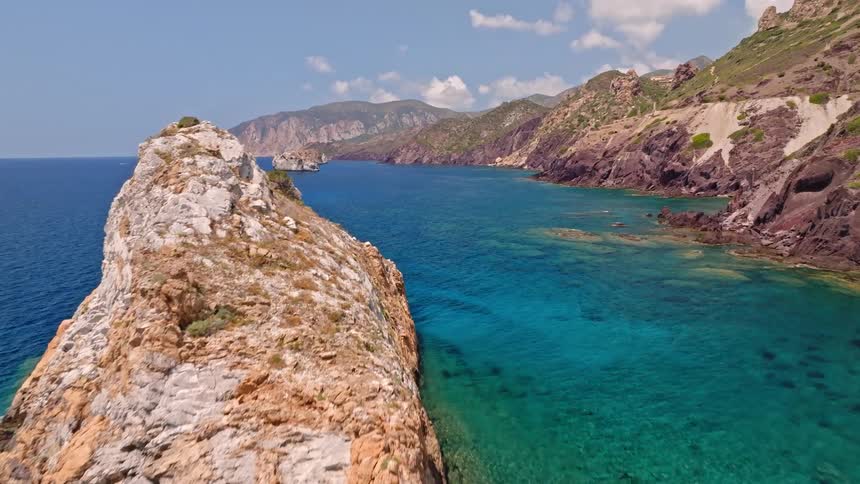 An aerial drone flies over the massive Pan di Zucchero sea stack, revealing the breathtaking turquoise waters and rugged coastline of Sardinia, Italy