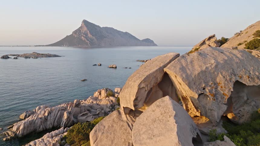 A slow aerial dolly shot reveals the beautiful, rocky coastline and clear blue sea of Sardinia at sunrise