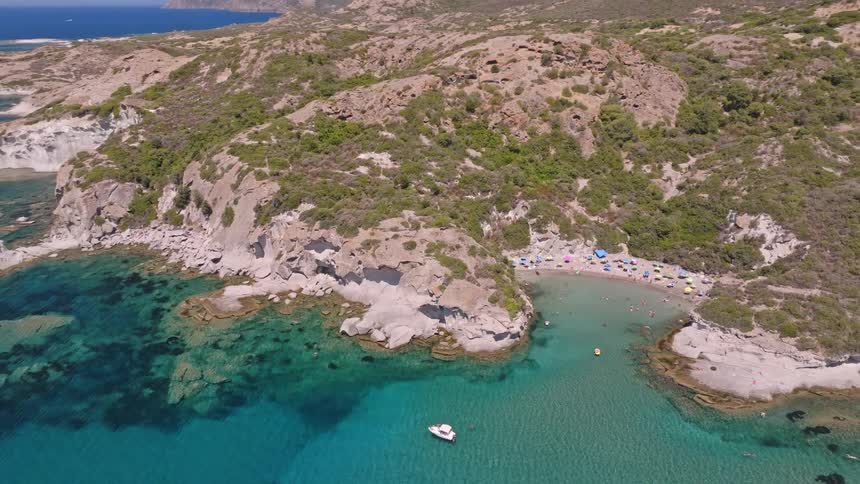 Aerial drone shot pulls back to reveal a stunning hidden cove with a sandy beach, turquoise water, and people enjoying a perfect summer day