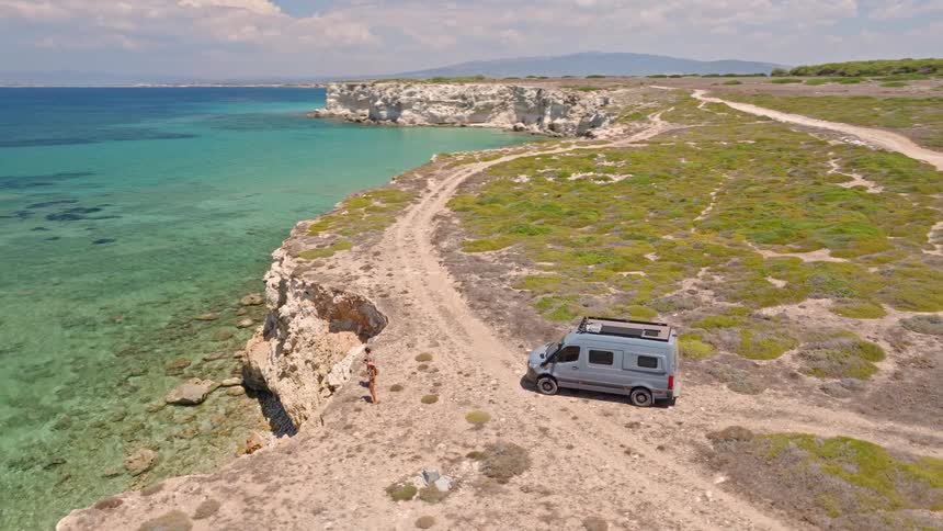 An adventurous couple enjoys the breathtaking coastal view from a clifftop where their camper van is parked during a summer road trip