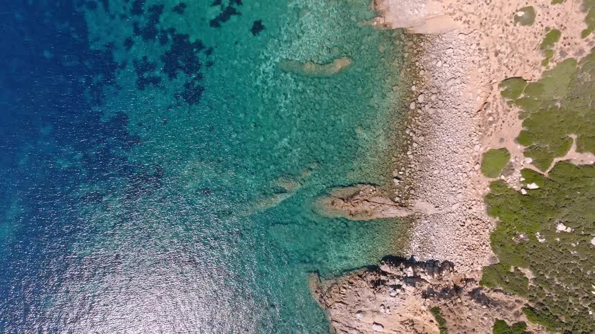 Top-down aerial view ascends over a stunning secluded cove with crystal clear turquoise water and a rocky shoreline