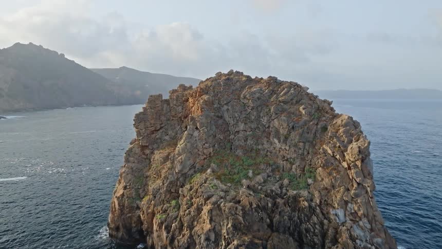 A dramatic aerial view pushes over a large sea stack revealing a vast ocean and a rugged coastline