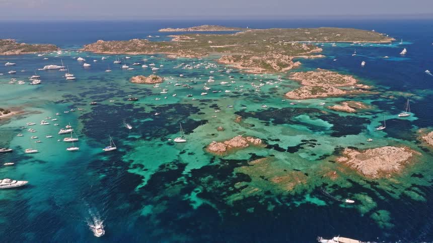 A breathtaking aerial shot captures a beautiful archipelago teeming with luxury yachts and boats in clear, vibrant turquoise waters
