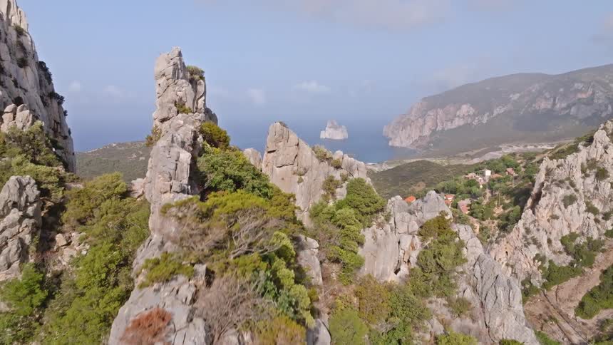Aerial drone shot rises above rugged coastal mountains to reveal the beautiful Pan di Zucchero sea stack on the Sardinian coastline