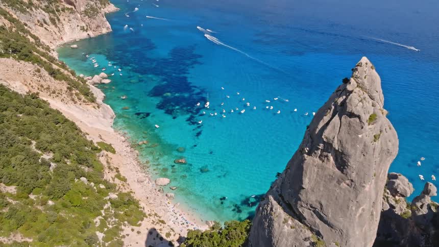 Spectacular aerial reveal of the famous Aguglia di Goloritzè spire overlooking the turquoise waters and beautiful coastline of Sardinia, Italy