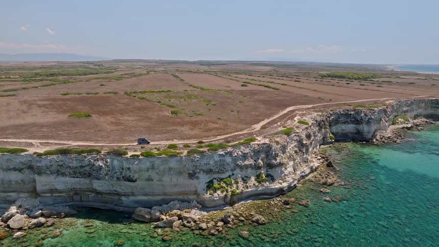 An epic aerial view pulls back to reveal a lone camper van parked on a scenic coastal road along a dramatic white cliff