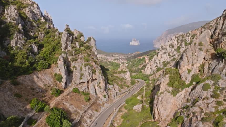 Stunning aerial footage reveals a winding road through a dramatic mountain pass leading to the beautiful Sardinian coastline and the Pan di Zucchero sea stack