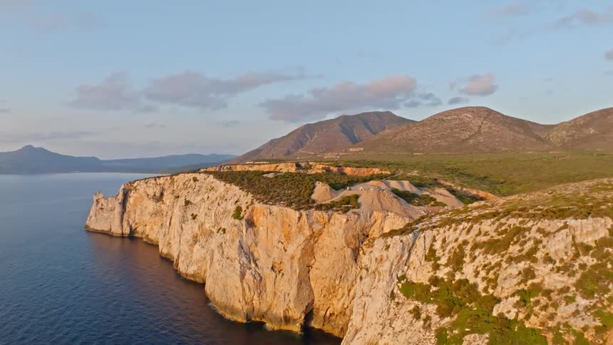 Stunning aerial footage rises over a rugged coastline, revealing dramatic cliffs illuminated by the golden sunset
