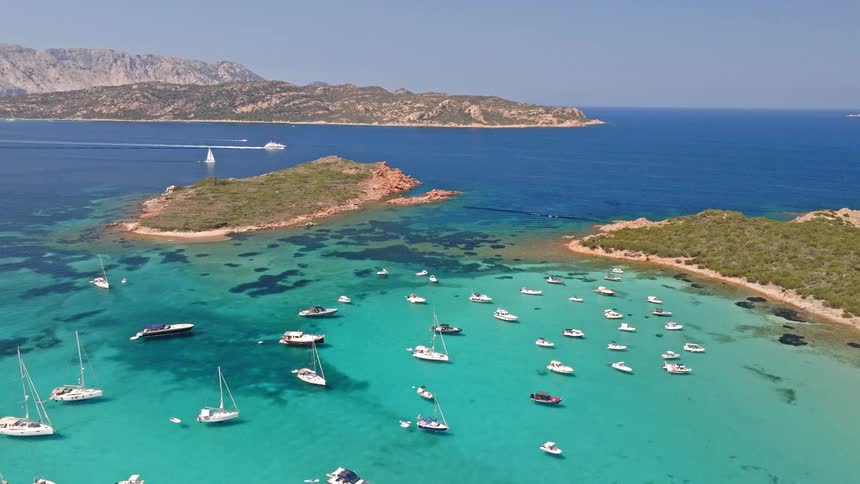 Breathtaking aerial panorama of numerous yachts and sailboats anchored in a pristine turquoise bay with mountainous islands in the background
