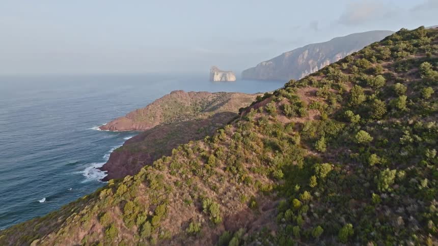Aerial drone footage reveals the stunning Pan di Zucchero sea stack off the rugged, green coast of Sardinia, Italy
