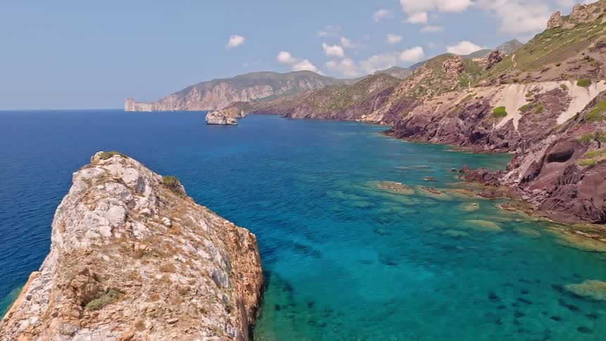 Breathtaking aerial view of a scenic coastline, featuring a prominent rock island, a small boat, and transparent turquoise sea