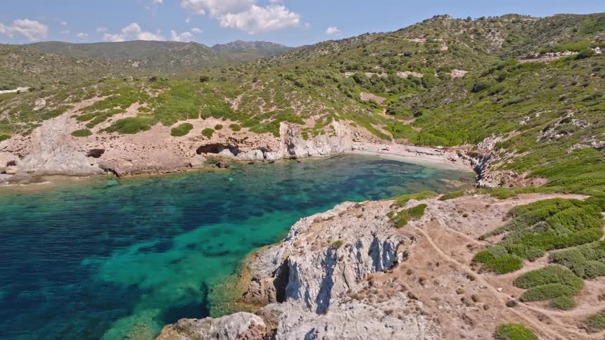 Ascending aerial view reveals a secluded, picturesque cove with a sandy beach and crystal-clear turquoise sea on a sunny day