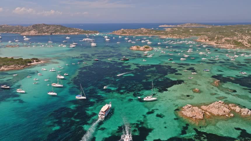 Stunning aerial view of numerous yachts and sailboats anchored in the breathtaking turquoise bay of the La Maddalena archipelago on a sunny day