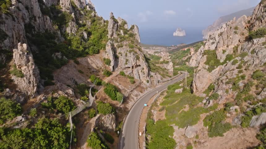An aerial view of a scenic coastal road winding through a rugged mountain canyon towards the deep blue sea on a sunny day
