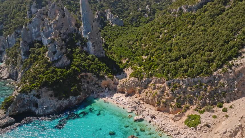 An aerial shot reveals the breathtaking beauty of Cala Goloritzè, a secluded beach with turquoise waters at the base of towering limestone cliffs
