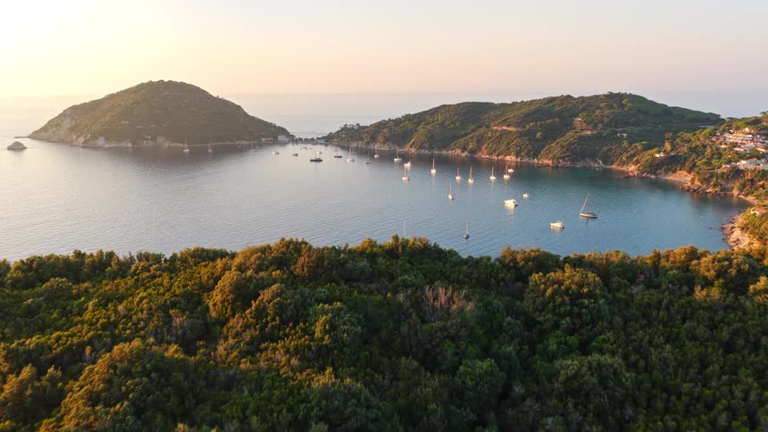 A stunning aerial view reveals sailboats anchored in a tranquil Mediterranean bay surrounded by lush green islands at golden hour