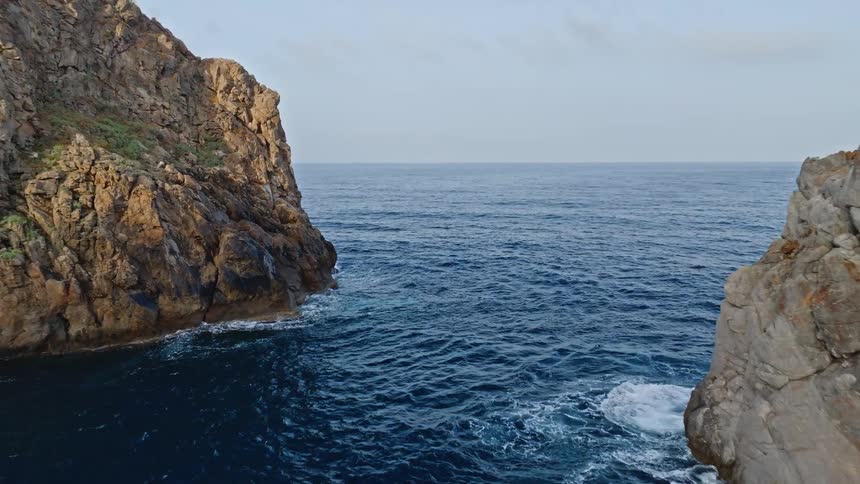 A stunning aerial pullback shot reveals two majestic sea stacks emerging from the deep blue ocean next to a rugged coastline