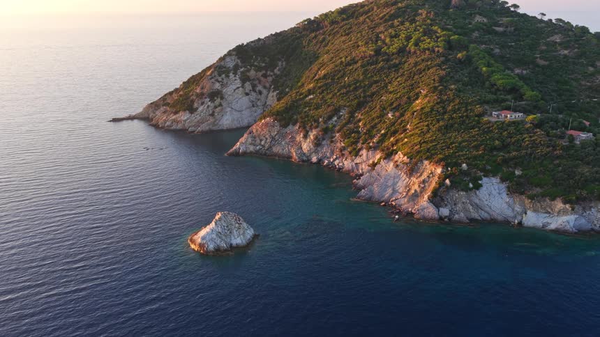 A majestic aerial view reveals a serene island and a small rocky islet surrounded by the deep blue sea during a breathtaking sunset