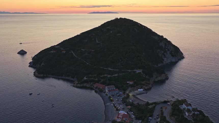 A breathtaking aerial view tilts up to reveal a stunning sunrise over the ocean behind a picturesque coastal village on an Italian peninsula