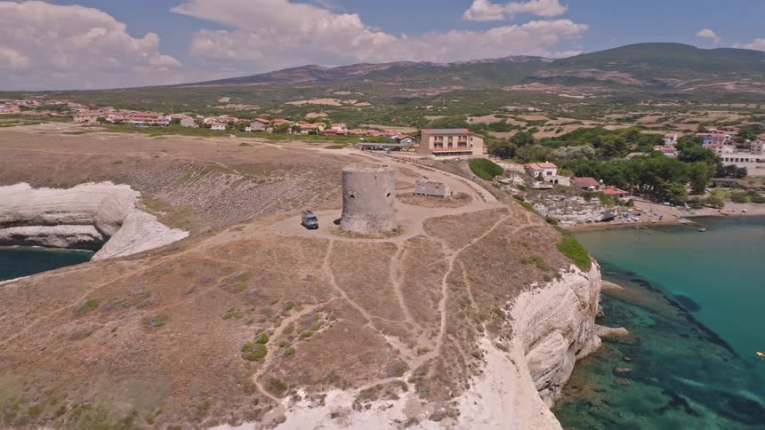 Slow aerial orbit of an ancient stone watchtower on a beautiful white cliff coastline overlooking the clear blue Mediterranean sea