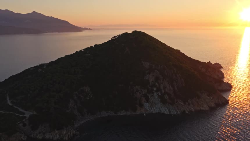 A breathtaking aerial timelapse captures the sun rising over a tranquil ocean, casting a golden glow on a lush, mountainous island