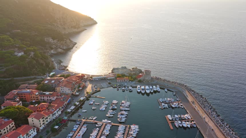Golden sunset illuminates a picturesque marina town nestled along a rugged coastline, an aerial perspective of docked boats and serene waters
