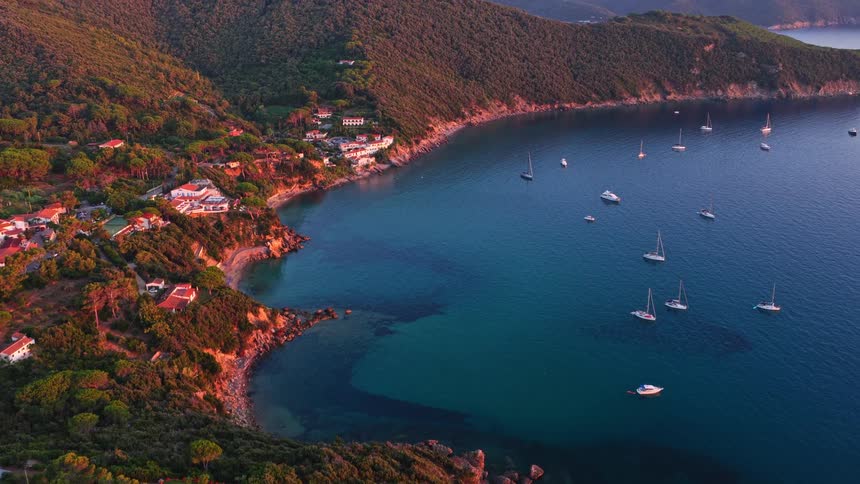 An idyllic aerial view captures a serene Mediterranean bay filled with sailboats and a charming coastal town during the warm glow of sunset