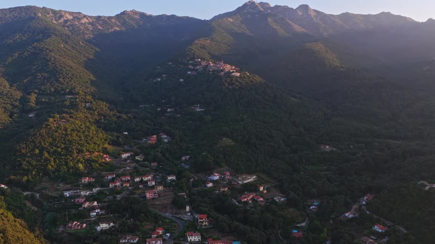 A scenic aerial shot reveals a charming European village nestled in a lush green mountain valley at sunrise