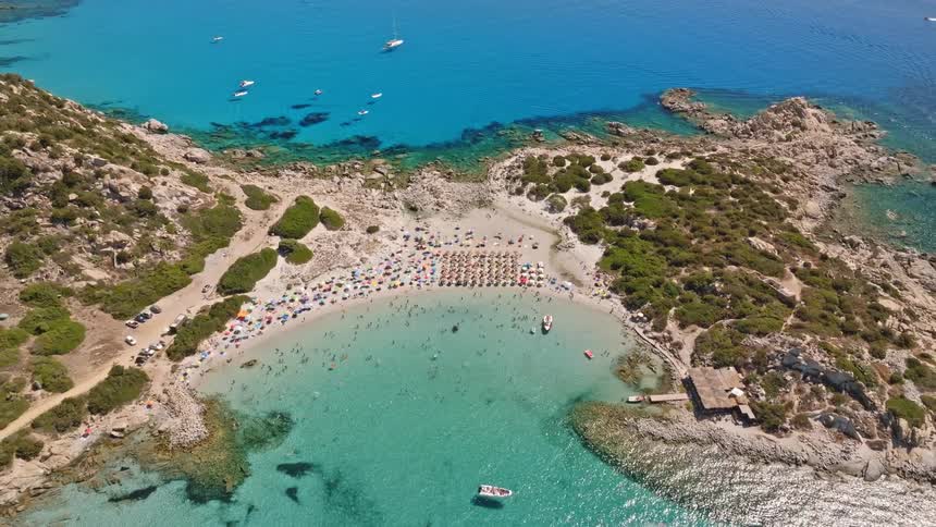 Breathtaking aerial view reveals a crowded beach in a stunning rocky cove with crystal clear turquoise water
