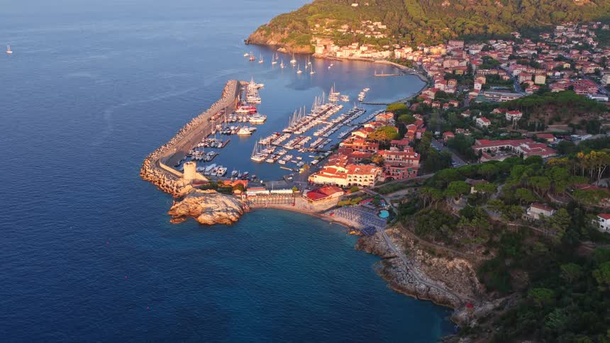 A stunning aerial view reveals a picturesque harbor and coastal town on the Mediterranean Sea, bathed in the warm golden light of sunrise