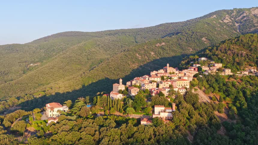 An aerial view captures the historic Italian village of Marciana on the island of Elba, nestled in the lush green mountains during a golden sunrise